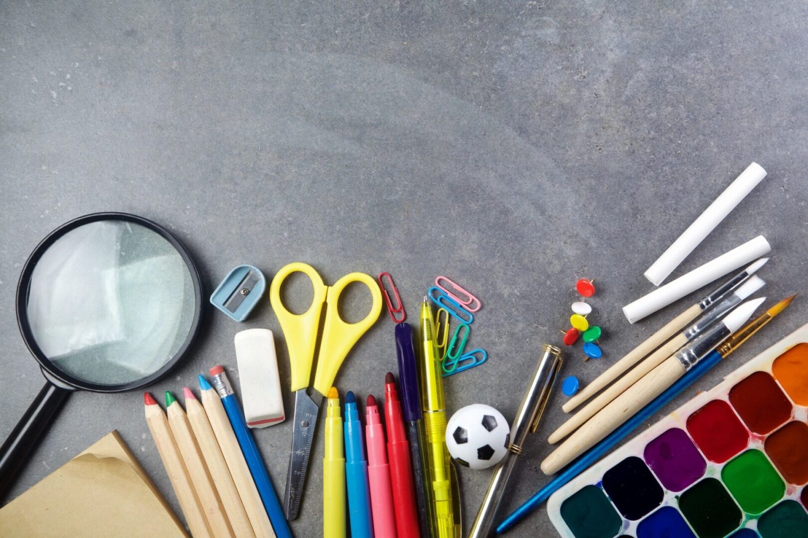 Colorful stationery including pencils, scissors, and markers on a gray surface.